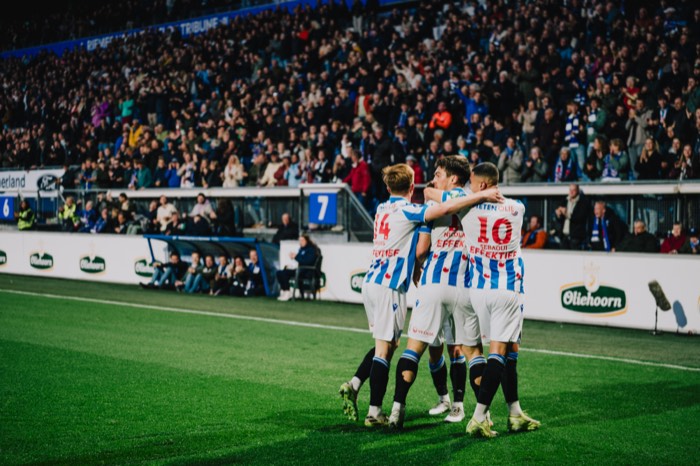 Fußballspieler von SC Heerenveen umarmen sich jubelnd auf dem Rasen vor einer Zuschauertribüne unter Flutlicht