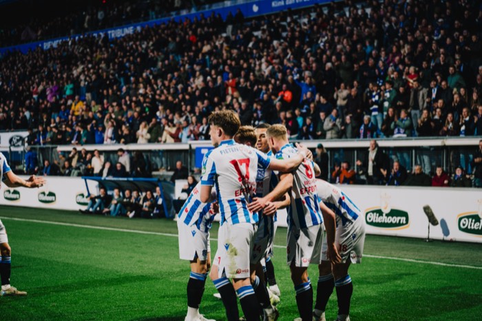 Blau-weiß gekleidete Fußballspieler umarmen sich jubelnd unter Flutlicht auf dem Rasen vor voll besetzten Rängen im Stadion