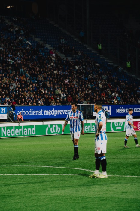 Drei Fußballspieler des SC Heerenveen stehen bei Flutlicht auf dem grünen Rasen vor voll besetzten Tribünen im Stadion