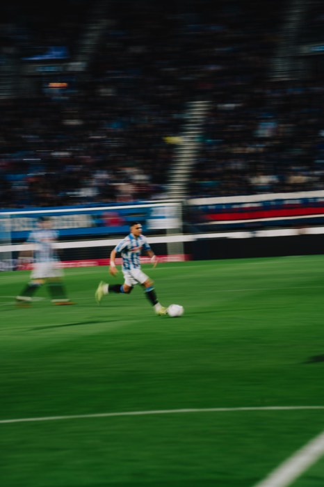 Ein Fußballspieler im blau-weiß gestreiften Trikot dribbelt bei Flutlicht mit dem Ball über den grünen Rasen im Stadion