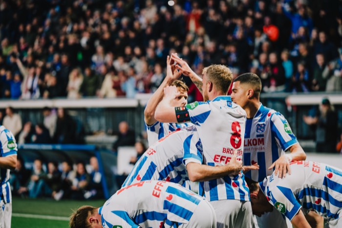 Fußballspieler im blau-weiß gestreiften Trikot jubeln gemeinsam unter Flutlicht vor vollen Rängen im Stadion
