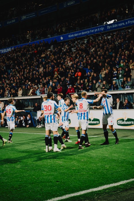 Fußballspieler in blau-weiß gestreiften Trikots jubeln auf dem Rasen vor voll besetzten Zuschauerrängen bei Flutlicht im Stadion