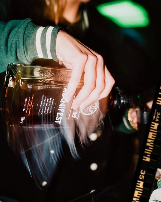 Eine Hand hält eine Flasche Jägermeister Manifest mit aufsteigendem Rauch in dunkler Clubumgebung bei gezieltem Lichtspot