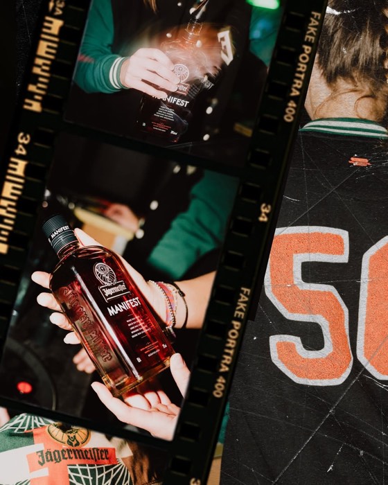 Hände präsentieren eine Flasche Jägermeister Manifest im gezielten Blitzlicht vor dunklem Hintergrund in analoger Filmoptik