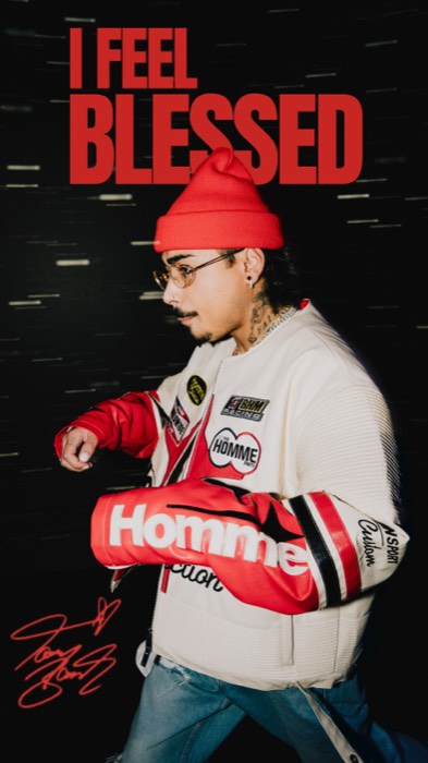 Tony Bauer geht im Blitzlicht in rot-weißer Jacke vor dunklem Hintergrund unter dem Schriftzug I FEEL BLESSED