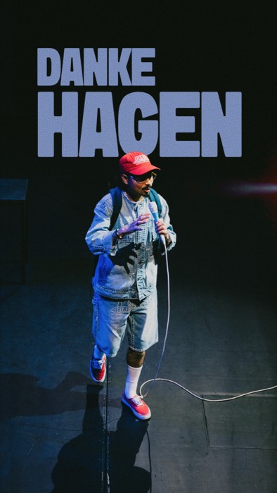 Tony Bauer spricht im Scheinwerferlicht auf einer dunklen Bühne ins Mikrofon unter dem großen Schriftzug DANKE HAGEN